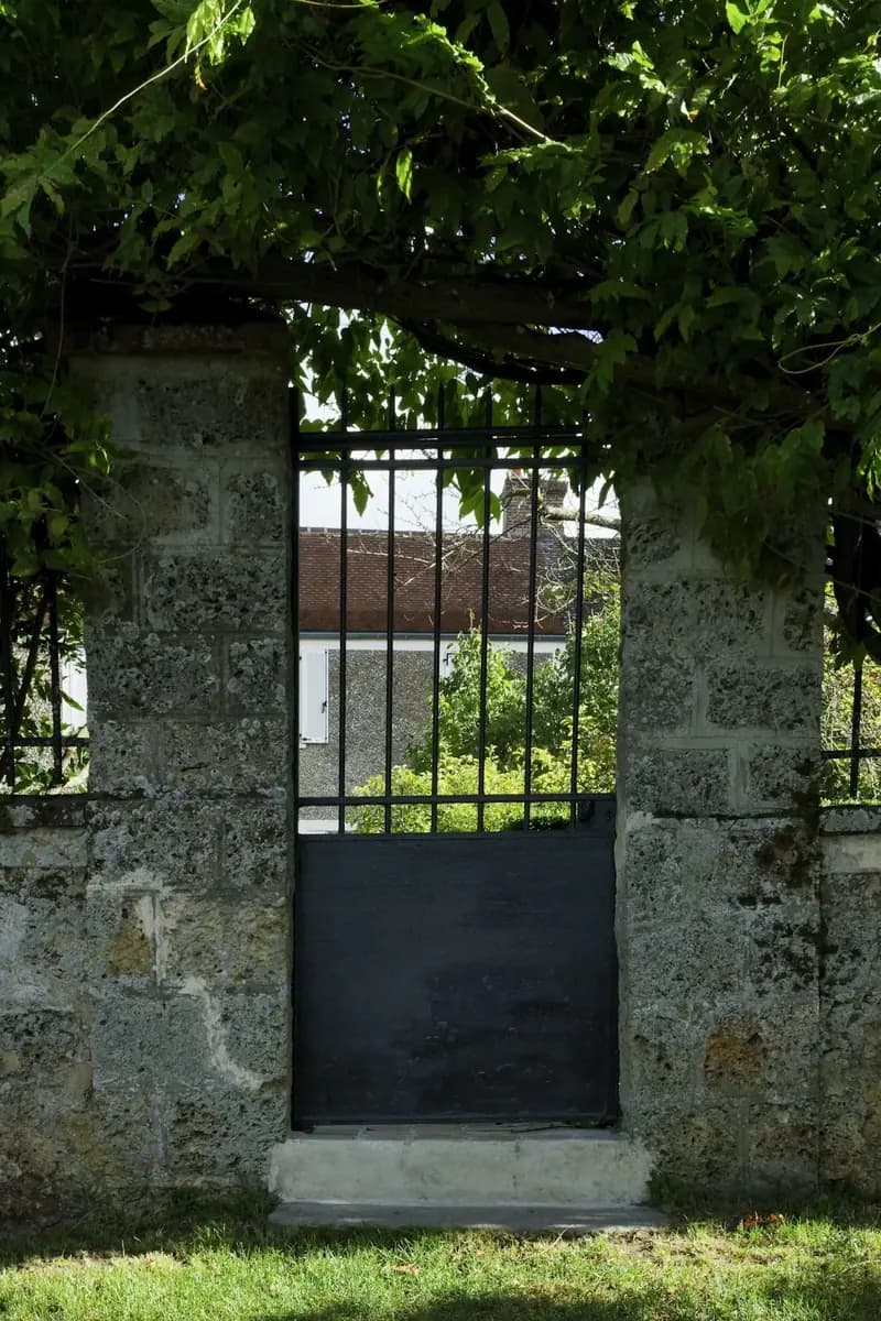 Black iron gate set into a stone wall, with greenery overhead.