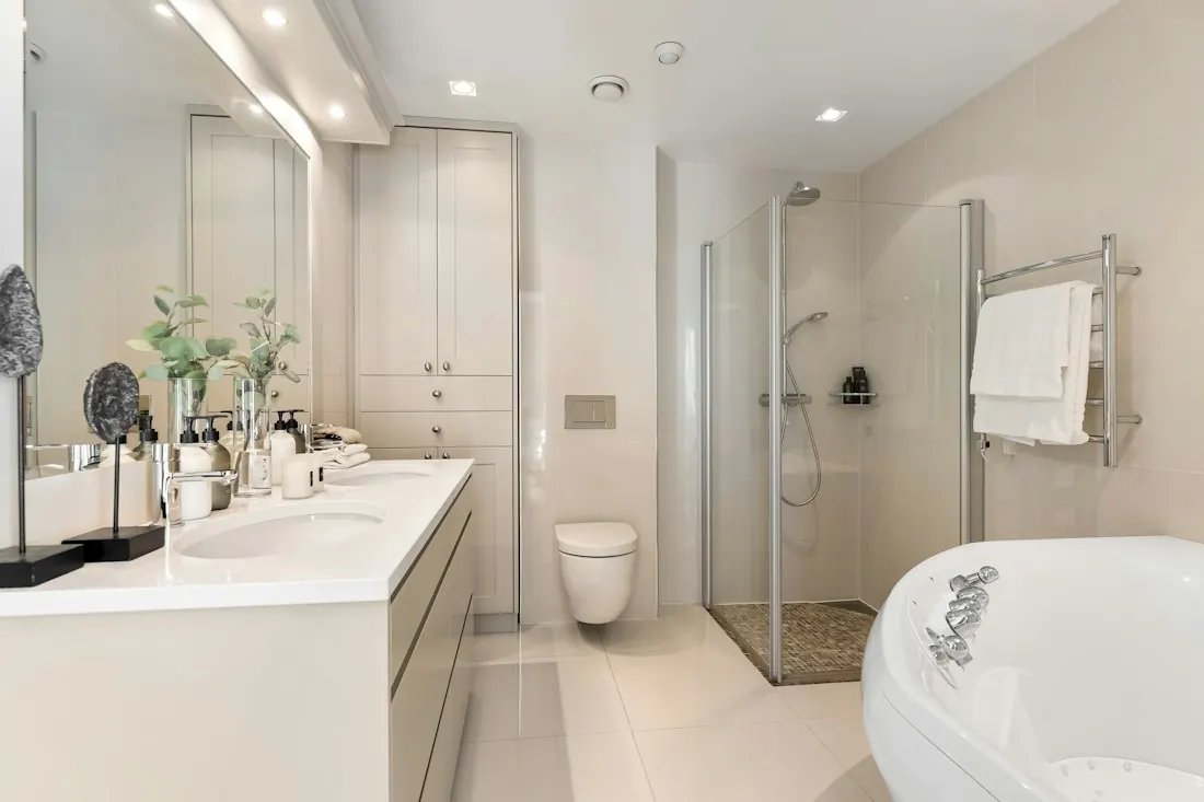 White bathroom with a freestanding tub, a long vanity with two basins, a glass shower and a heated towel rail.