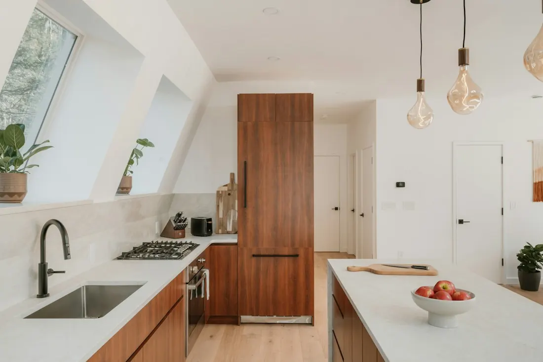 Bright kitchen with white counters, a black faucet, tall walnut cabinetry and pendant lights over an island.