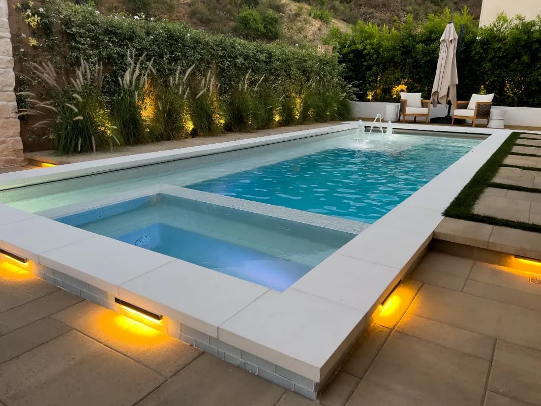 Long lap pool and adjoining spa at dusk, with underwater lighting and lit deck edges.