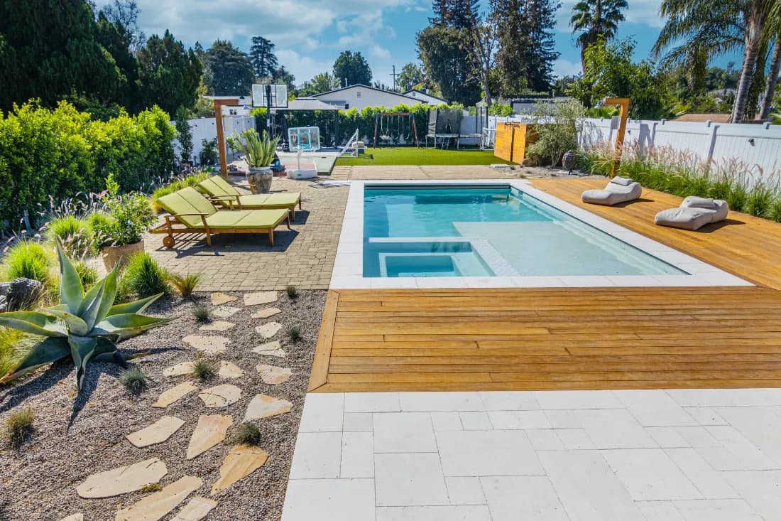 Backyard pool and spa bordered by a wood deck, stone paving and desert planting.