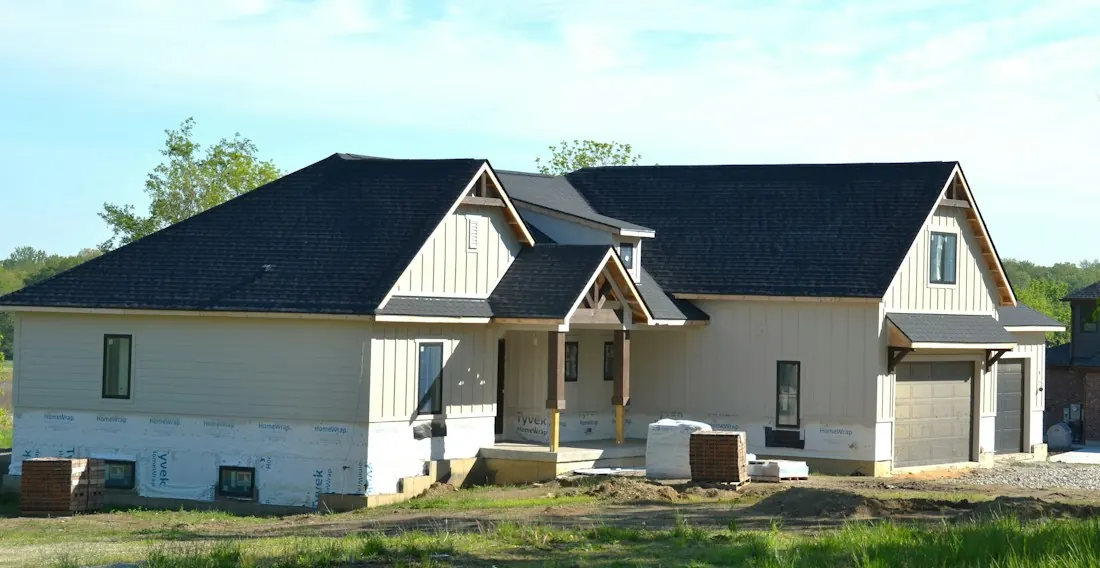 Newly built house with a dark shingle roof, pale siding and a two-car garage.