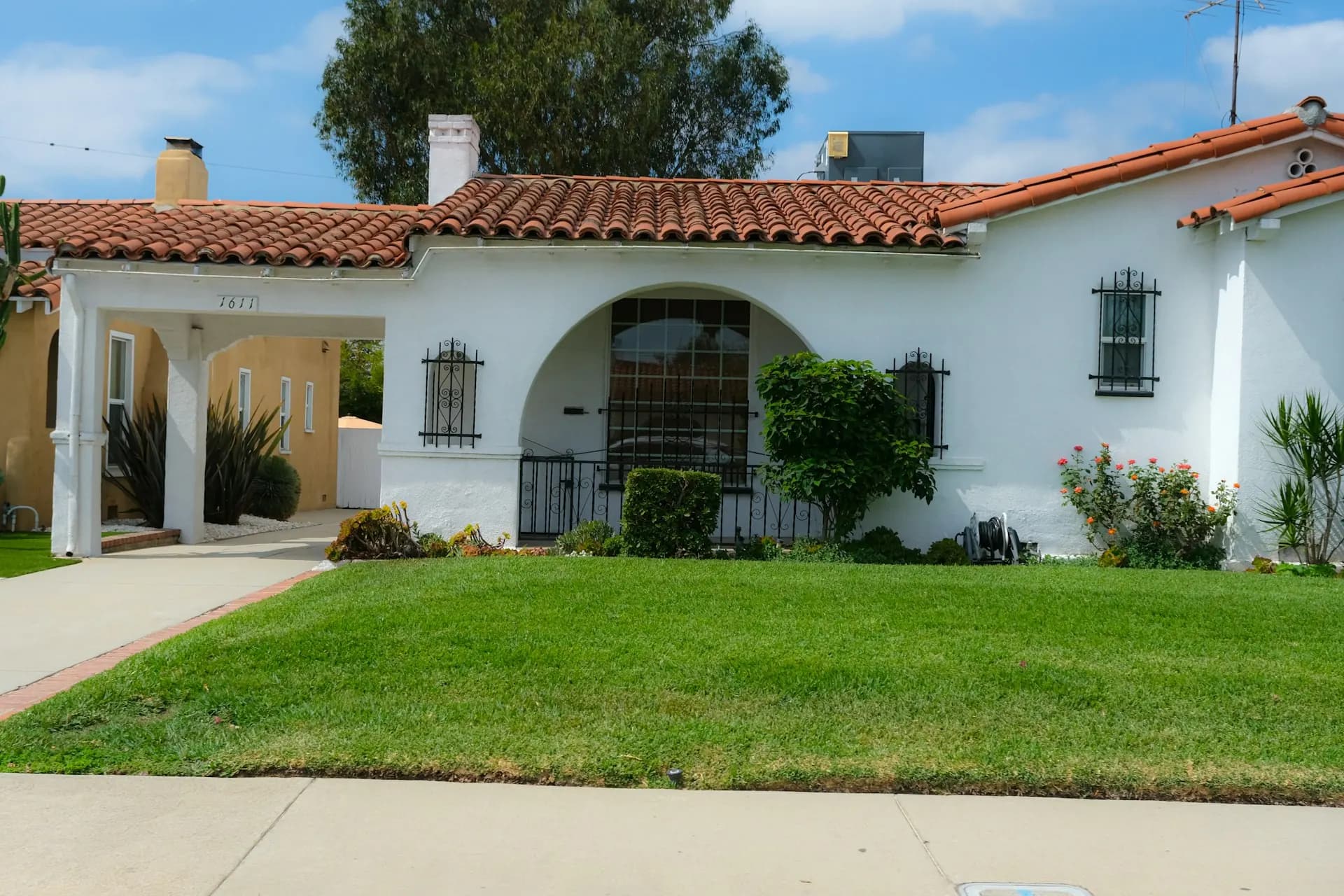 Single-storey white stucco house with a red clay tile roof, an arched entry and a front lawn.