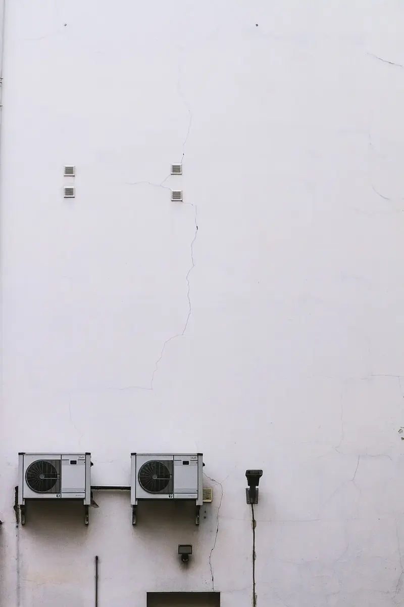 Two outdoor air-conditioning units mounted low on a plain white wall.