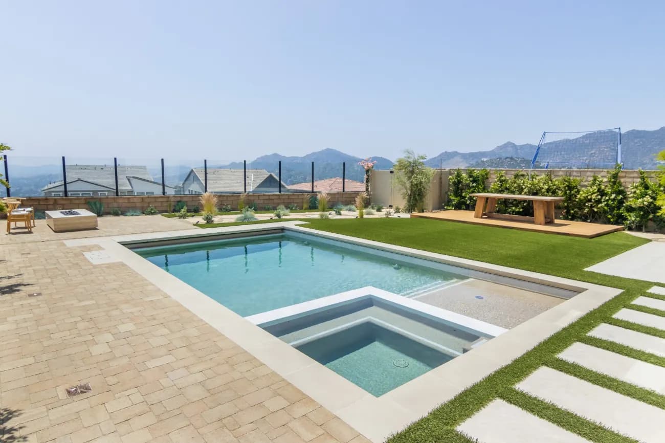 Pool and spa with a wide paved deck and turf, overlooking distant mountains.