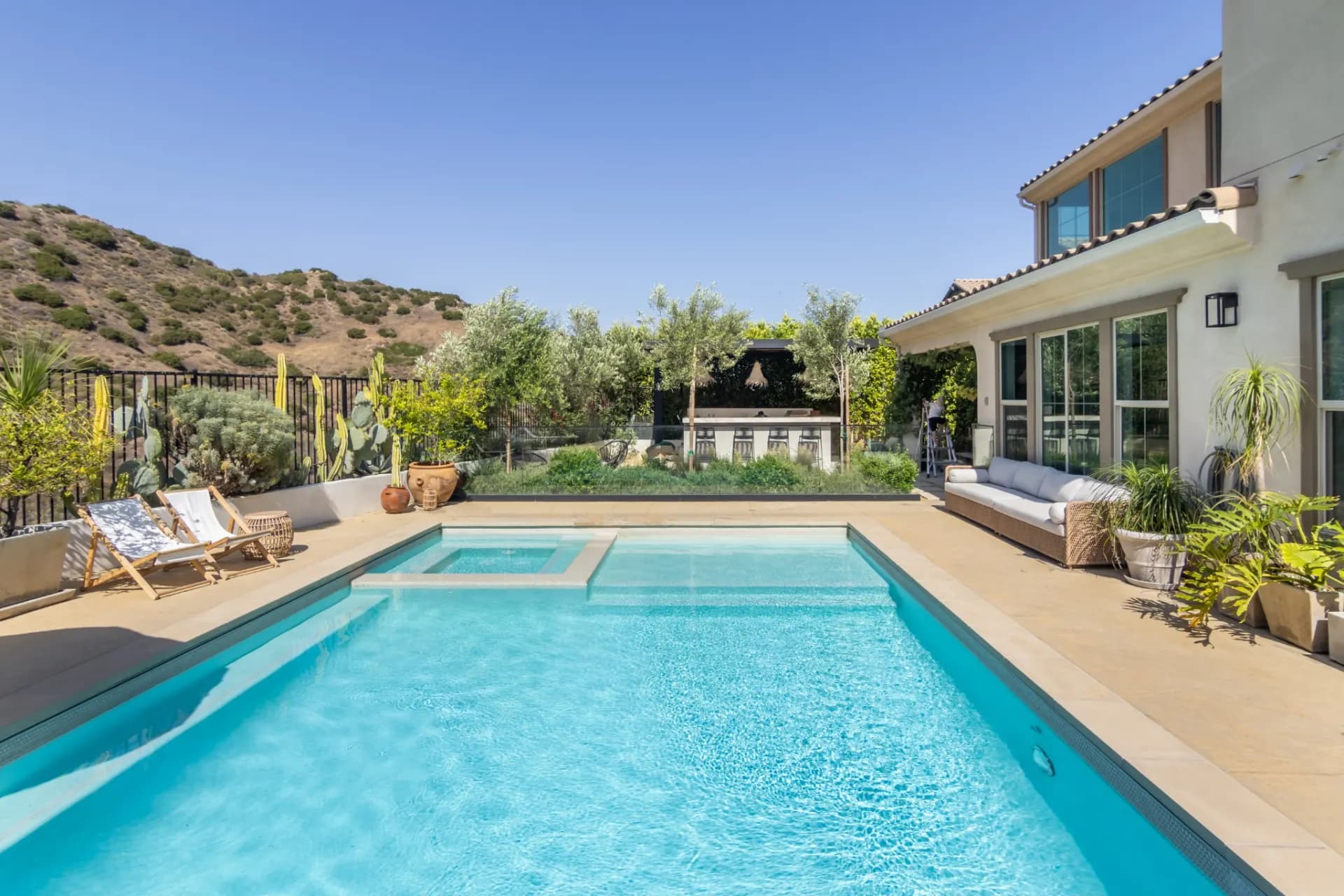 Swimming pool and spa on a hillside property, with lounge chairs, patio umbrellas and open desert hills behind.